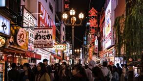 Crowd of tourists strolling down one of the streets in Osaka's Dotonbori area. Cityscape by night with lots of billboards and lights.