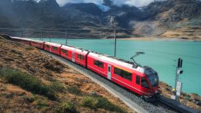 Red train is moving along railway in swiss alps mountain. Autumn