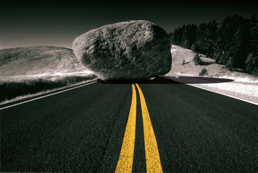 Yellow lane divider leading up to a boulder blocking the road