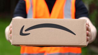 A man delivering an Amazon box with the Amazon smile logo in the UK