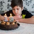 Teen boy looks thoughtfully at cake with candles on twelfth day of birth