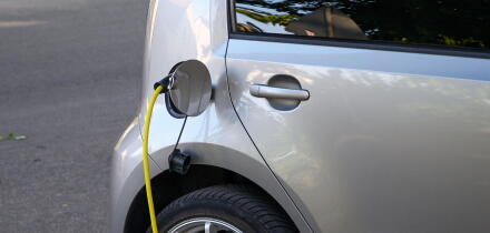 Silver electric car charging with a yellow cable plugged into its port.