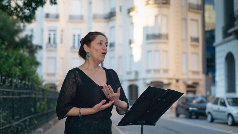 Soprano sings opera on an elegant street with a music stand