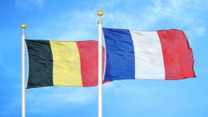 Belgium and France two flags on flagpoles and blue cloudy sky