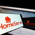 Smartphone with logo of British repairs company HomeServe plc on screen in front of business website. Focus on center-left of phone display.