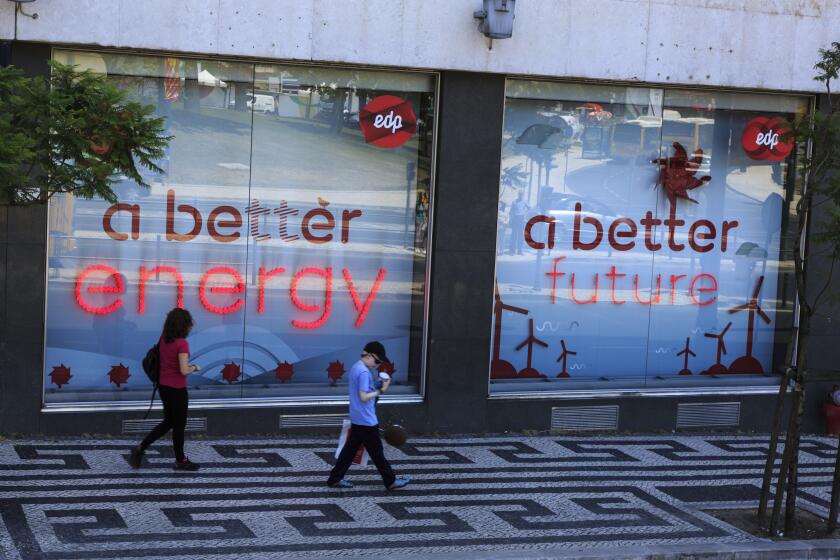 Two people walking past signs in the store window of EDP power company depicting a better energy a better future, Lisbon Portugal