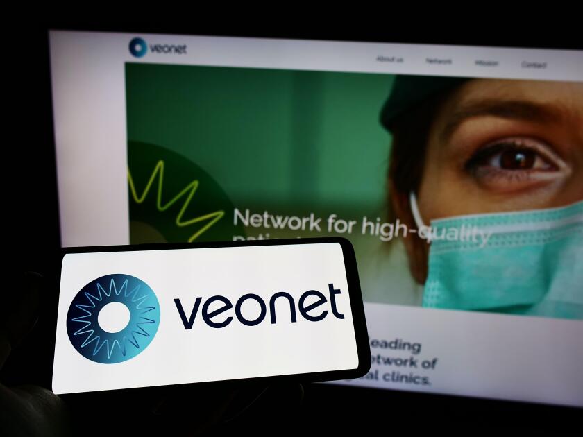 Person holding mobile phone with logo of ophthalmological clinic network Veonet GmbH on screen in front of web page. Focus on phone display.