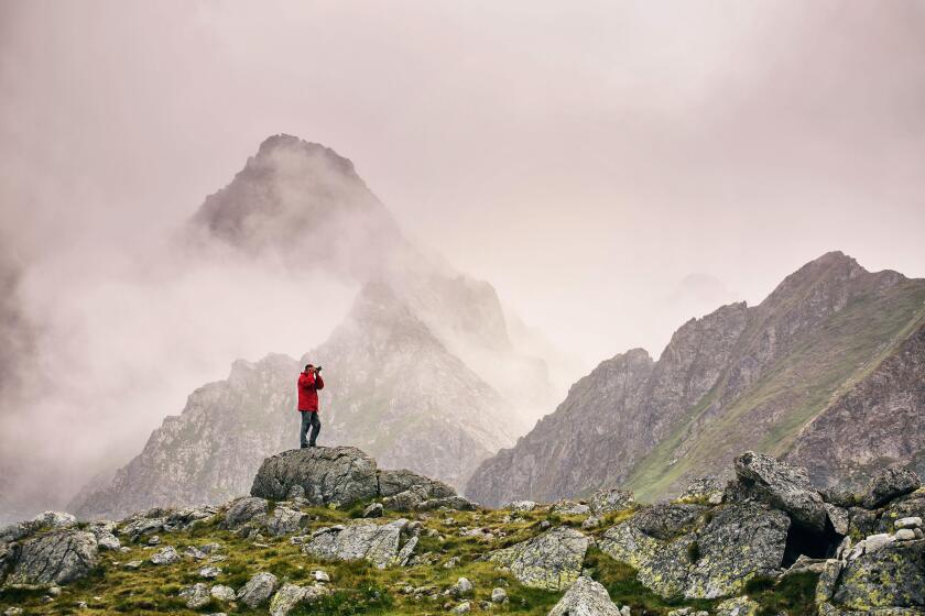Hiker with camera standing on top of a mountain