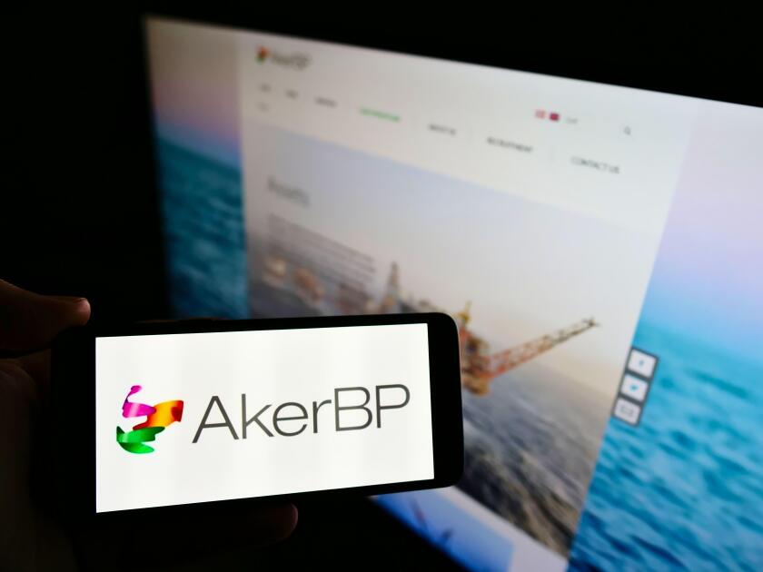 Person holding mobile phone with business logo of Norwegian oil and gas company Aker BP ASA on screen in front of web page. Focus on phone display.