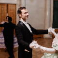 Portrait of smiling gentleman wearing classic tailcoat dancing with young lady during debutante ball in palace, copy space