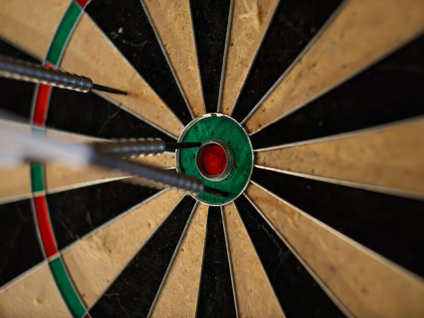 Darts in a dartboard close up. The bullseye is the target but it was missed. The objective is to hit the center. This leisure activity is a party game