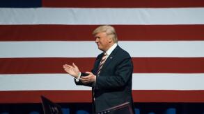 Republican Presidential Nominee Donald Trump walking on stage applauding the crowd near the American Flag.