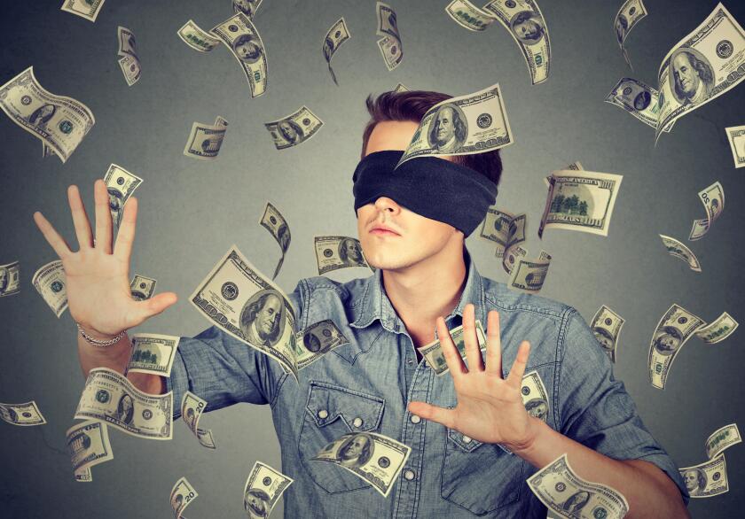 Blindfolded young businessman trying to catch dollar bills banknotes flying in the air isolated on gray wall background. Financial corporate success o