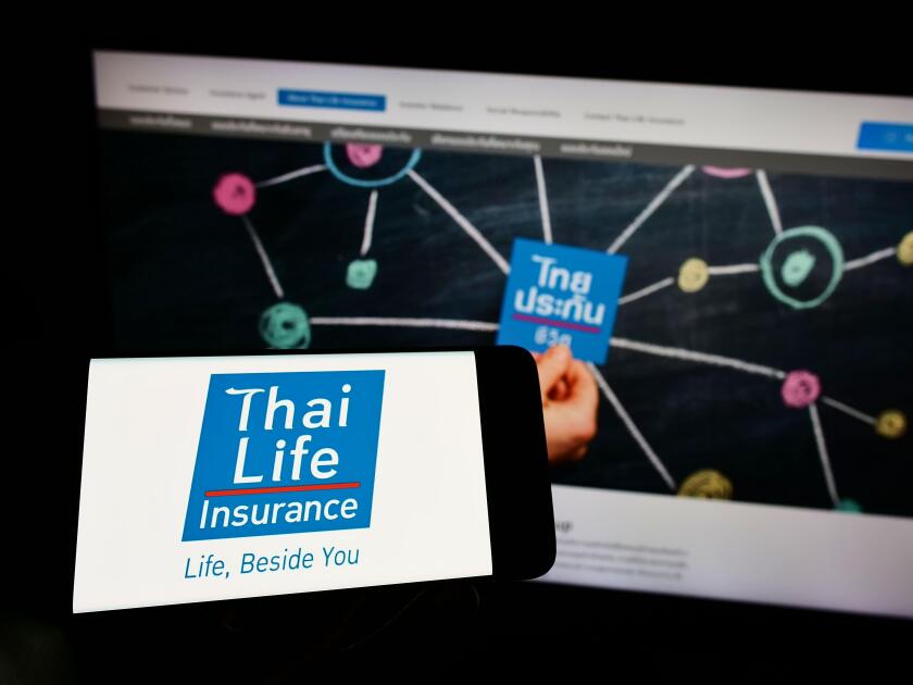 Person holding smartphone with logo of company Thai Life Insurance Public Co. Ltd. on screen in front of website. Focus on phone display.