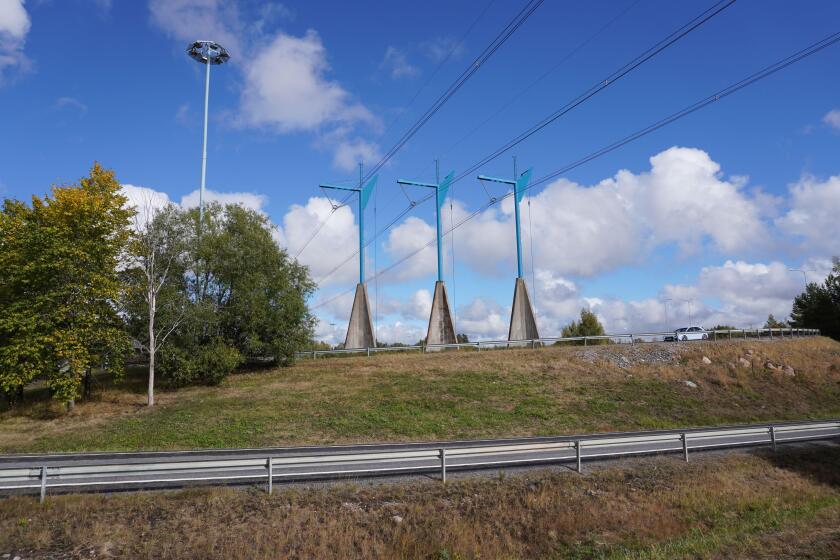 A scenic view of modern transmission towers on a green hill along the road on a sunny day