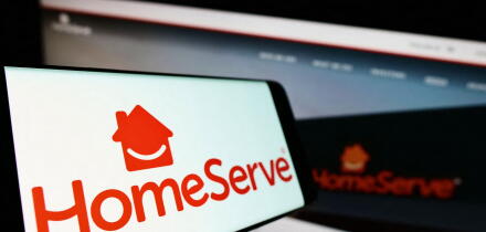 Smartphone with logo of British repairs company HomeServe plc on screen in front of business website. Focus on center-left of phone display.