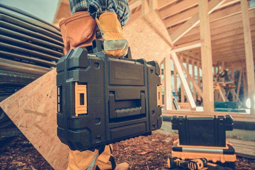 Closeup of Toolbox with Professional Carpentry Tools and Equipment in a Hand of Contractor Entering the Building Site to Start His Work. Industrial Th