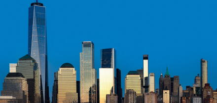 The massive scale of the downtown New York City skyline, with the sun reflecting off the glass and steel architecture.