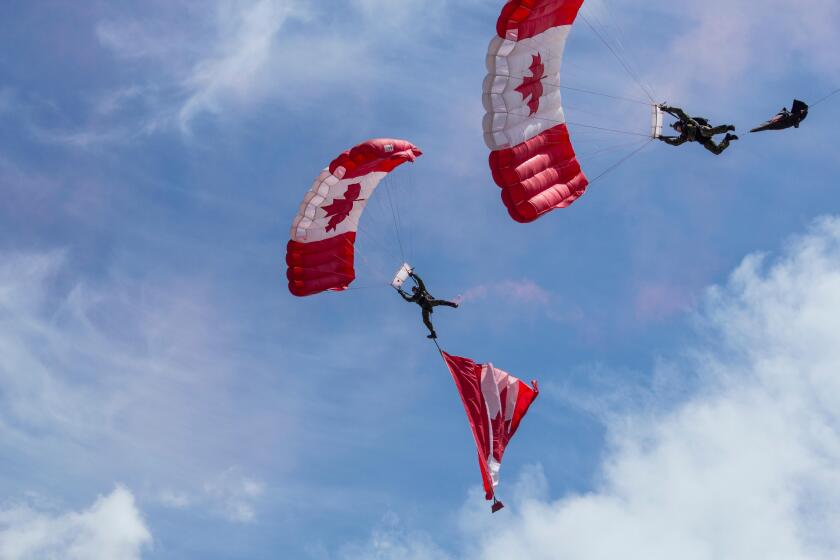 Canadian parachute jumpers perform at the Calgary Stampede and Rodeo. Red and white parachutes with maple leaf design against blue sky with wispy clou