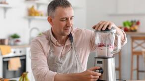 Mature man making fruit smoothie with blender in kitchen