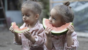 Little caucasian twins girls eating watermelon. Children sisters sitting together. Family time.