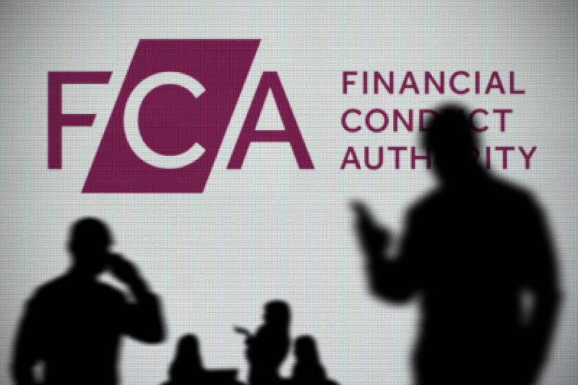 The FCA logo is seen on an LED screen in the background while a silhouetted person uses a smartphone in the foreground (Editorial use only)