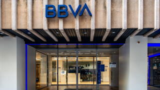 The BBVA bank branch in Cartagena, Spain, featuring a concrete ribbed facade, blue logo, and glass sliding doors illuminated by purple neon lights.