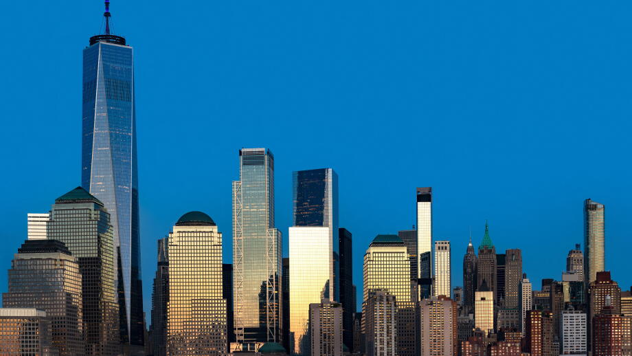 The massive scale of the downtown New York City skyline, with the sun reflecting off the glass and steel architecture.