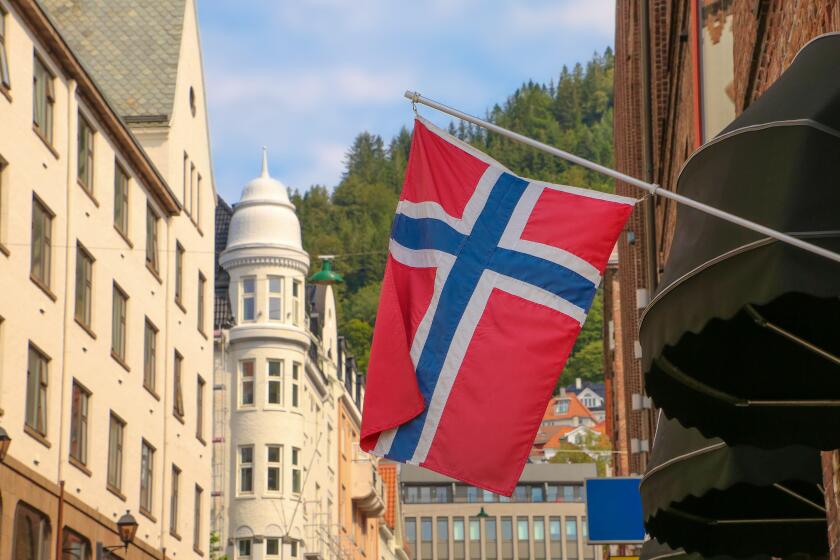 Typical street in Bergen, historic architecture, a Norweigan flag and  mountain of Floyen in the background on a summer day. Norway.