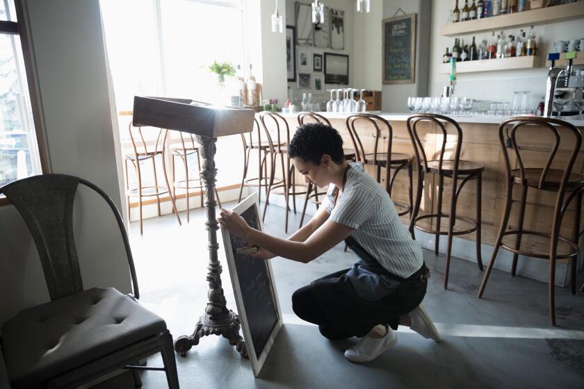 Young woman small business owner preparing menu on cafe blackboard