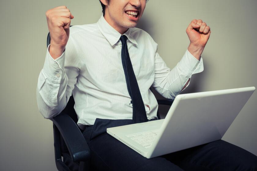 A young businessman is sitting in an office chair and is getting excited about his laptop