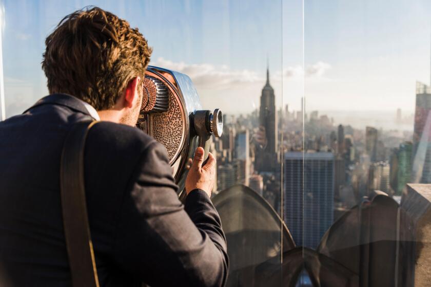 USA, New York City, man looking through coin-operated binoculars on Rockefeller Center observation deck