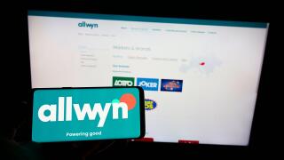 Person holding cellphone with logo of company SAZKA Entertainment AG (Allwyn) on screen in front of business webpage. Focus on phone display.