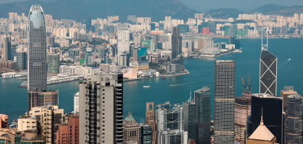 The skyline of Victoria Bay features impressive skyscrapers and busy harbor activities with a clear blue sky above.