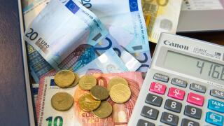 Various Euro notes and coins with a calculator, diary and laptop computer.