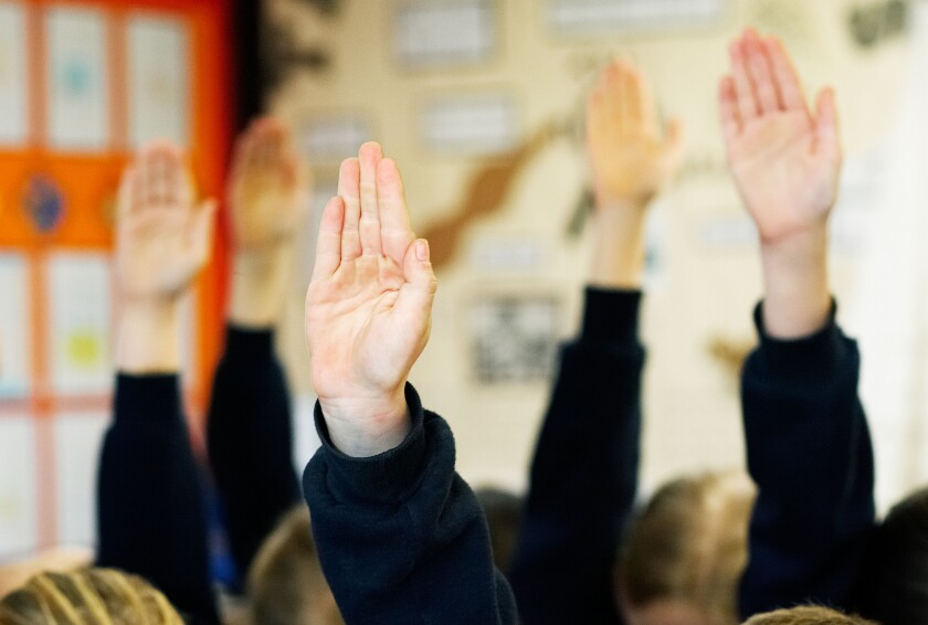 School children with hands up in the air wanting to answer a question