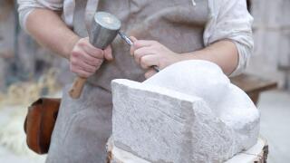 Close up of young sculptor hands working on his marble sculpture in his workshop with hammer and chisel