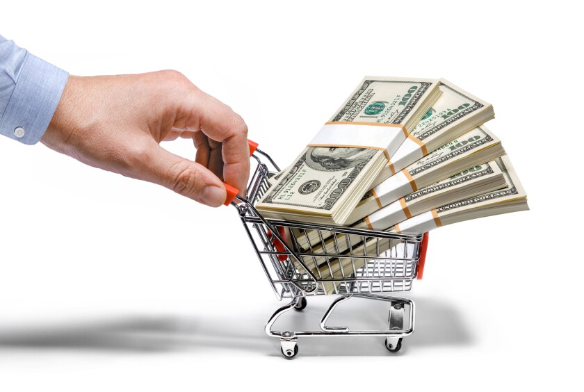 Businessman's hand holds grocery cart full of money stacks