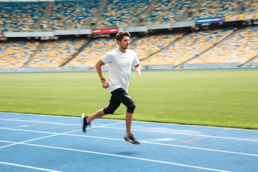 Side view of a young professional sprinter running on racetrack