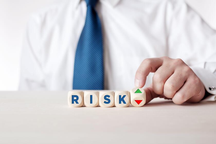 Businessman hand turns a wooden cube with the arrows symbolizing the risk level is high or low.
