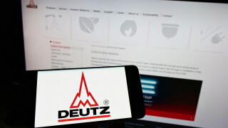Person holding cellphone with logo of German engine company Deutz AG on screen in front of business webpage. Focus on phone display.