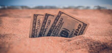 Money dolars half covered with sand lie on sandy beach near sea ocean waves on sunny summer day close-up. Money grows out of the ground. Concept finance money holiday relax vacation.