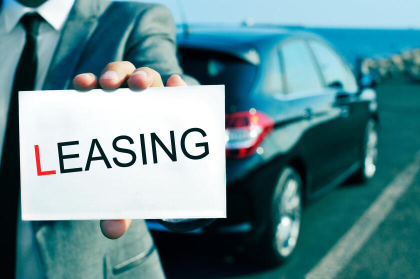 man in suit holding a signboard with the word leasing written in it, with a black car in the background