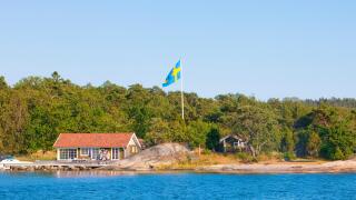 Sweden, Stockholm - House on island in archipelago with swedish flag on pole.