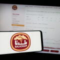 Person holding mobile phone with logo of Qatari dairy and food company Baladna in front of business web page. Focus on phone display.