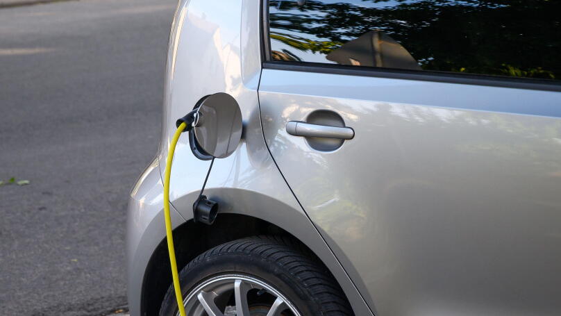 Silver electric car charging with a yellow cable plugged into its port.