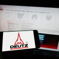 Person holding cellphone with logo of German engine company Deutz AG on screen in front of business webpage. Focus on phone display.
