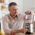 Mature man making fruit smoothie with blender in kitchen
