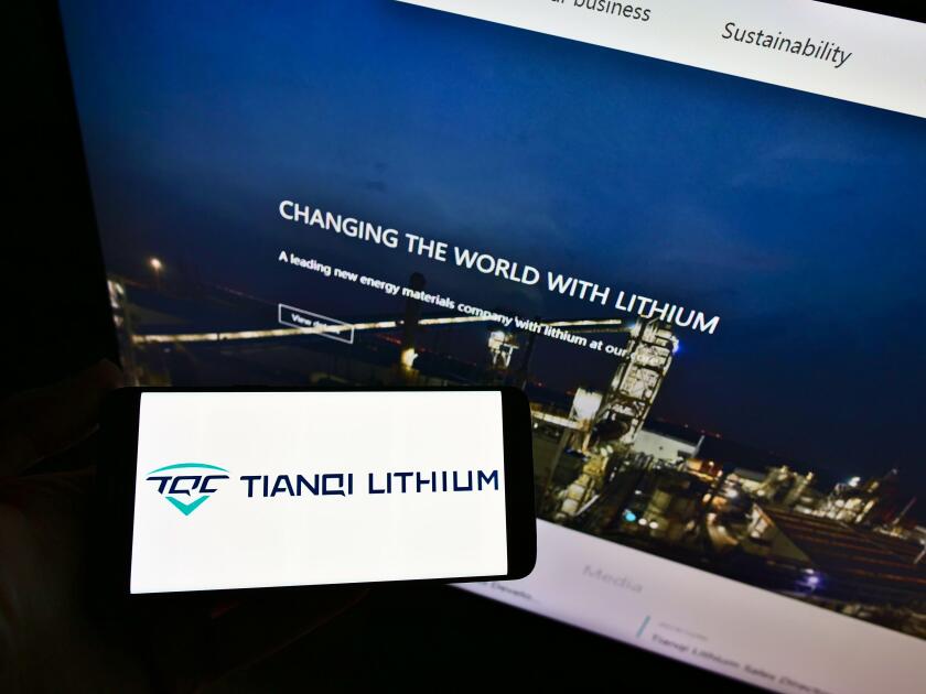 Person holding smartphone with logo of Chinese manufacturing company Tianqi Lithium Corp on display in front of web page. Focus on phone screen.