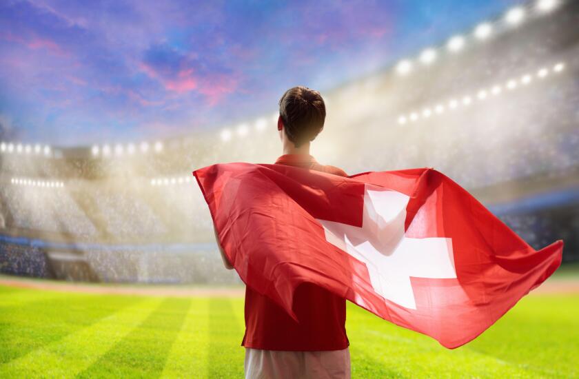 Switzerland football supporter on stadium. Swiss fan on soccer pitch watching team play. Young player with flag and national jersey